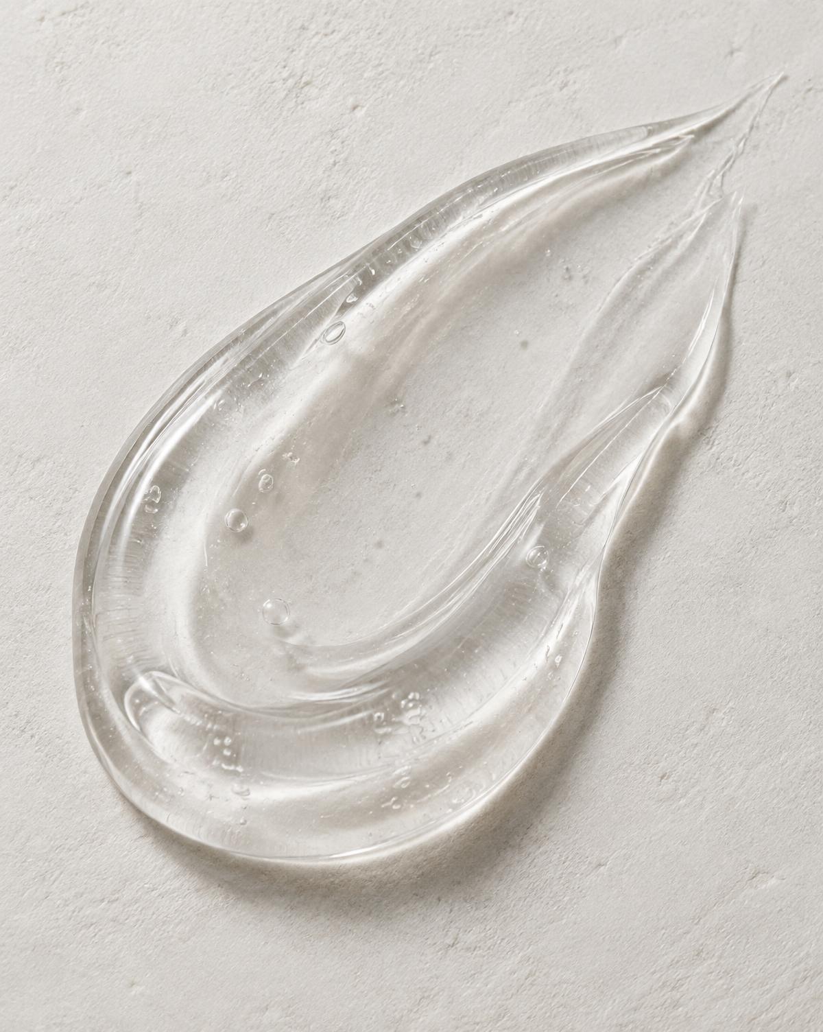 Macro detail of a clear skincare gel texture on a pale plaster surface